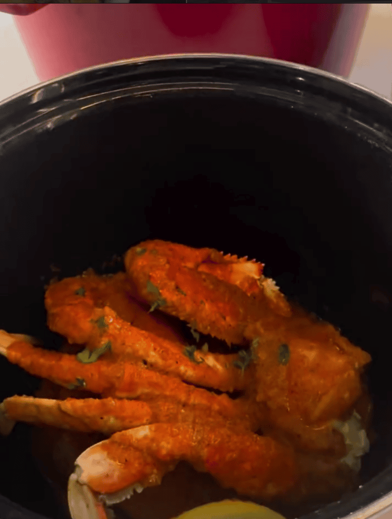 Golden-brown fried chicken pieces cooking in a black pot or slow cooker, shot from above in close-up detail.