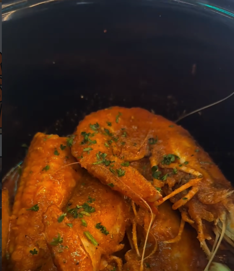Two whole cooked lobsters garnished with herbs sit in a dark cooking pot.