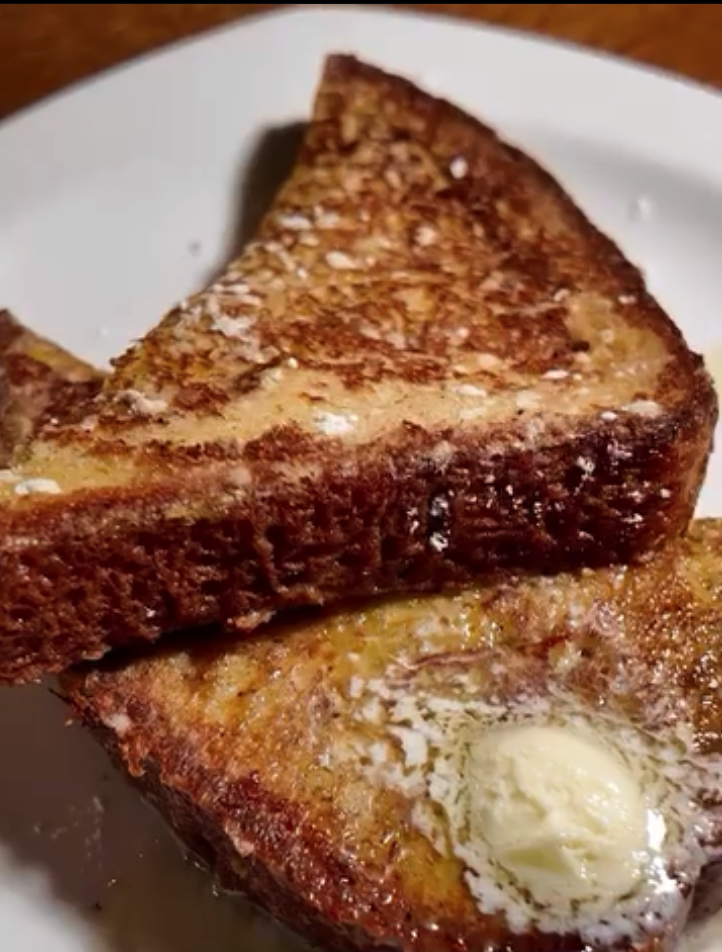 Golden-brown French toast slices topped with butter and cinnamon sugar served on a white plate.