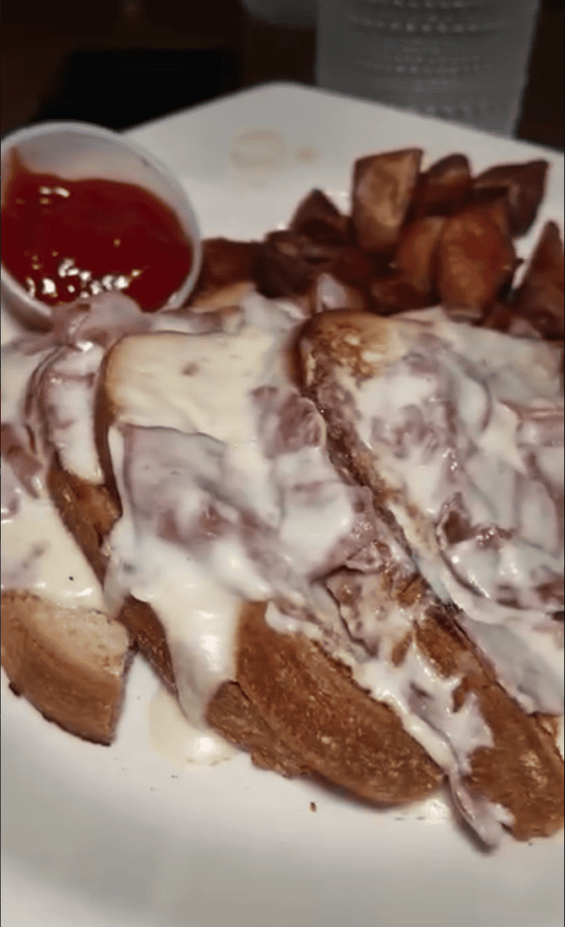 A plated dessert featuring sliced bread with white cream topping and crispy bacon strips, served with grapefruit and sauce on a white plate.