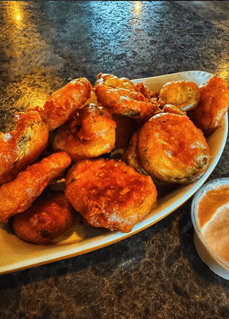 A close-up overhead view of crispy golden-brown fried chicken pieces arranged on a white plate with a small bowl of sauce on a dark speckled countertop.
