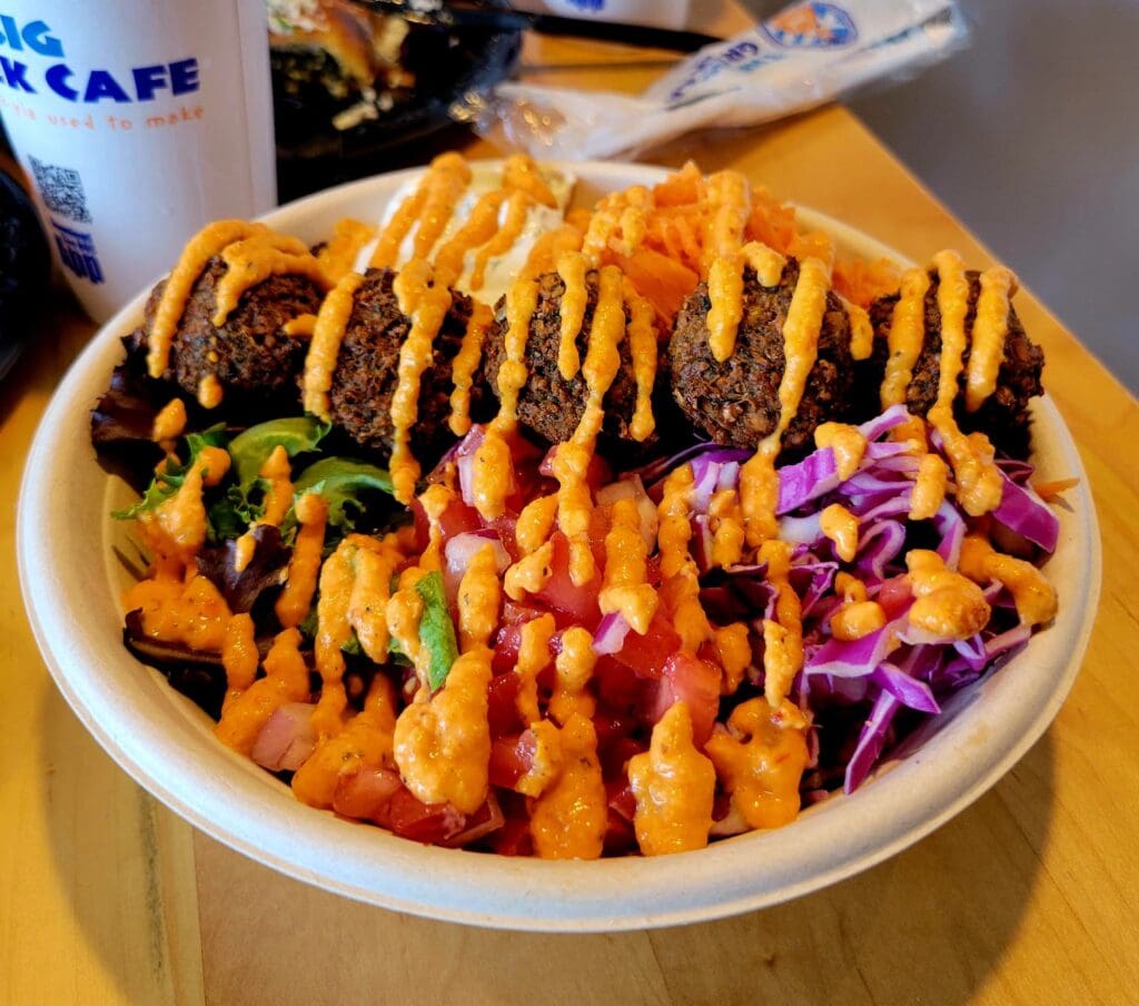 An overhead shot of loaded fries topped with melted cheese sauce, fresh vegetables, and purple cabbage served on a white plate at what appears to be a casual dining establishment.