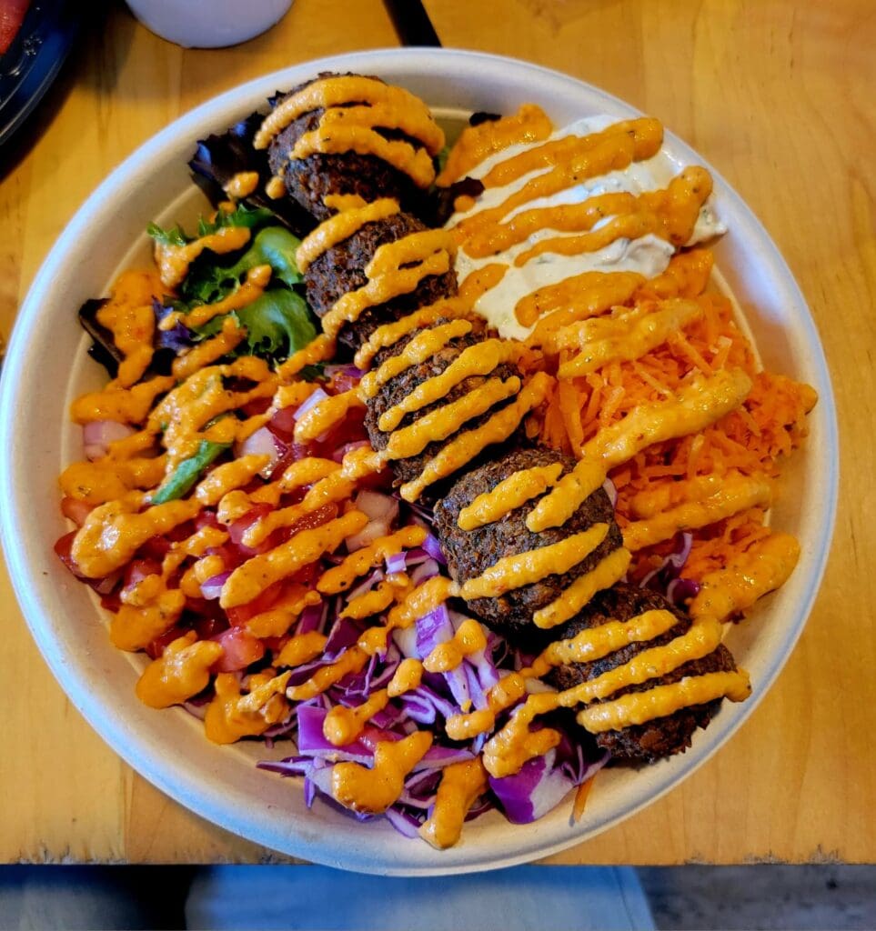 An overhead view of a white plate filled with colorful gourmet hot dogs topped with various condiments including drizzled sauces, purple onions, and green garnishes.