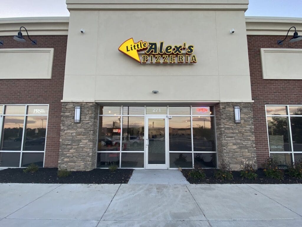 A daytime exterior view of a restaurant storefront with brick and stone facade, featuring a gold-lettered sign and glass entrance doors.