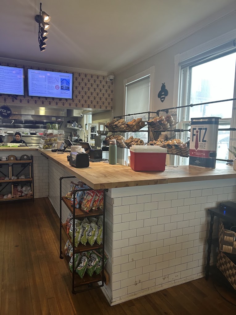 A modern coffee shop interior featuring a white tile counter, espresso machine, pastry display, and large windows with natural light.