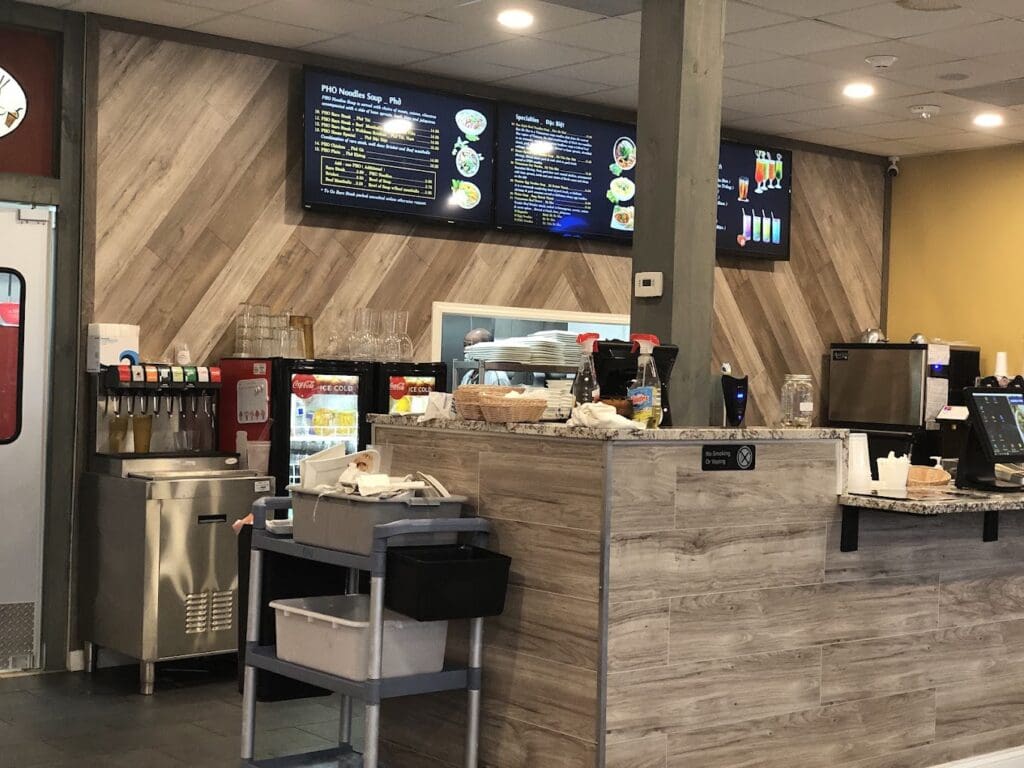 A modern coffee shop interior featuring a wooden service counter with menu boards, pastry displays, and professional espresso equipment in a contemporary cafe setting.