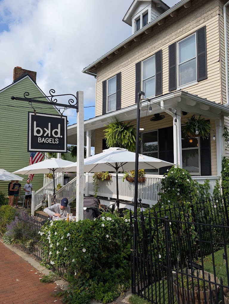A charming historic storefront restaurant with outdoor patio seating, featuring a cream-colored facade with black shutters and fresh green ivy accents.