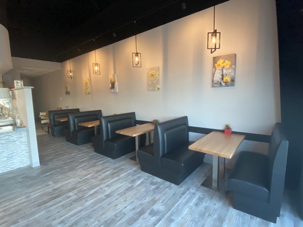 A modern restaurant interior with booth seating, wooden tables, and decorative pendant lighting in a warm, neutral color scheme.