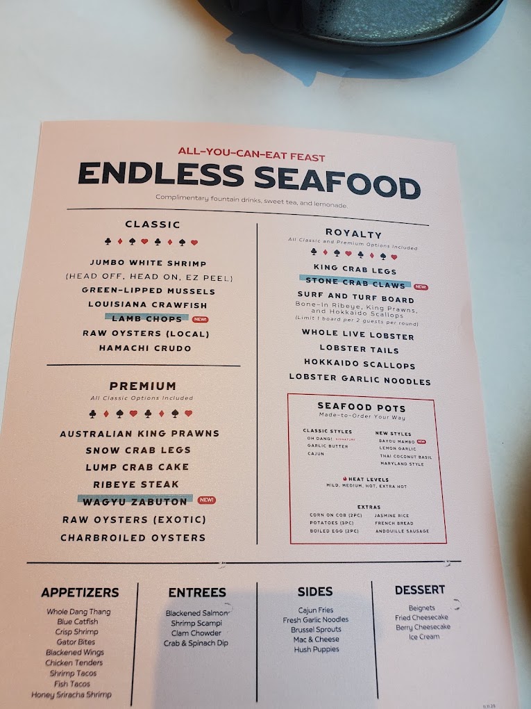 A printed restaurant menu for 'Endless Seafood' displayed flat on a light surface, featuring sections for classic dishes, proteins, appetizers, entrees, seafood, and desserts.