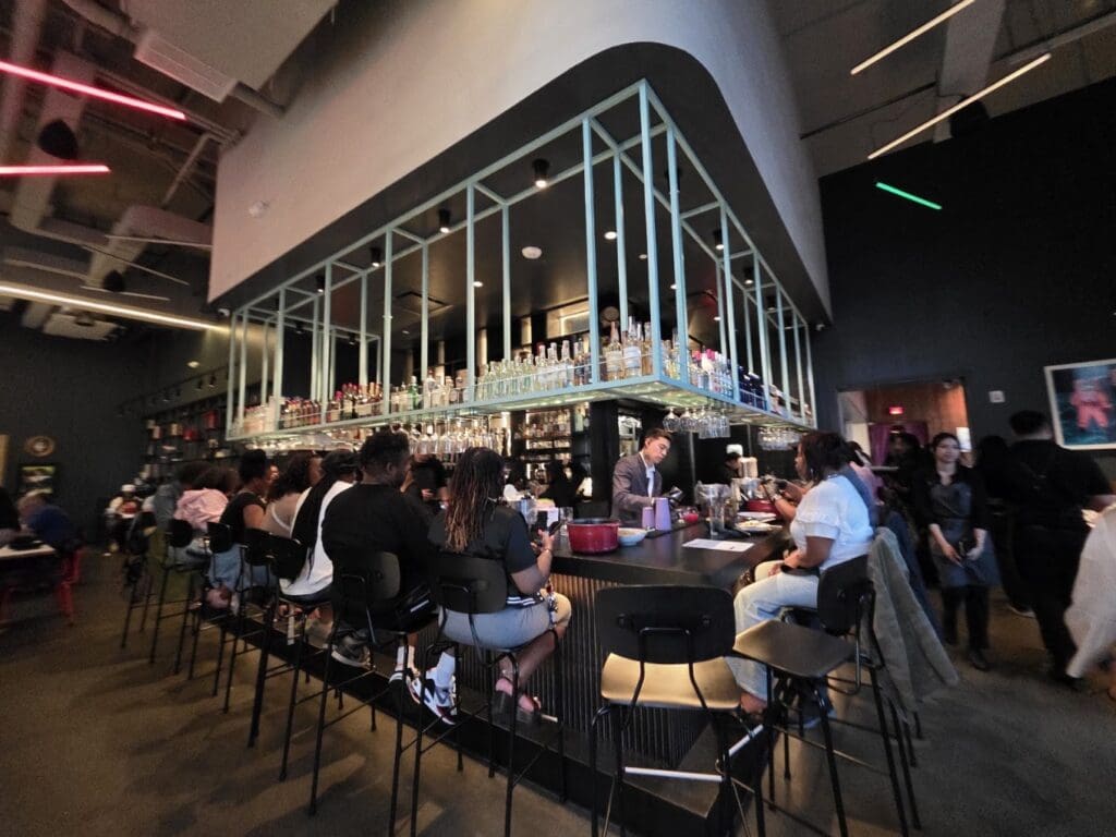 An evening gathering at a modern wine bar or restaurant venue with multiple attendees seated and mingling in a contemporary interior space.
