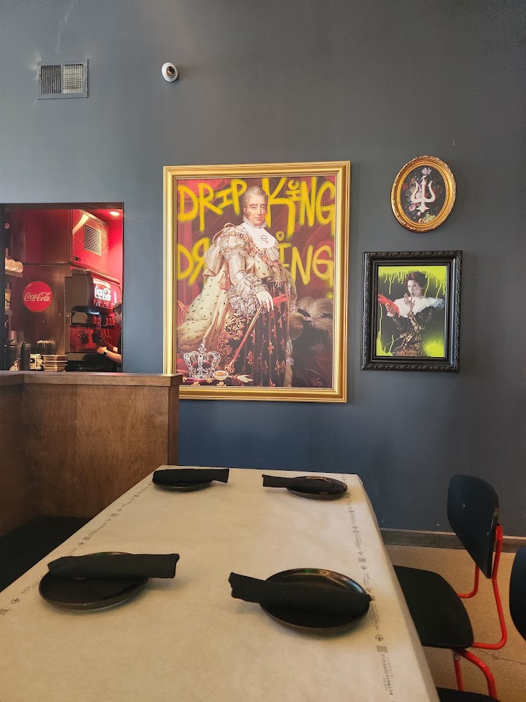 A minimalist workshop or creative space featuring a wooden desk with headphones, gray walls decorated with vintage posters and framed artwork.
