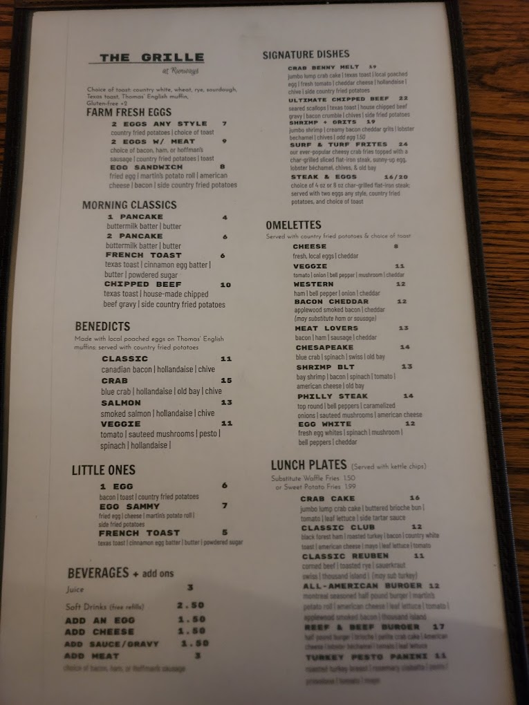A laminated restaurant menu photographed flat on a wooden surface, displaying various food and beverage options organized in sections.