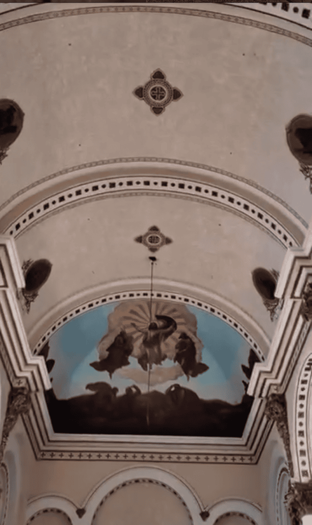 An ornate church ceiling featuring a barrel vault with religious frescoes, decorative crosses, and classical architectural detailing in cream and earth tones.