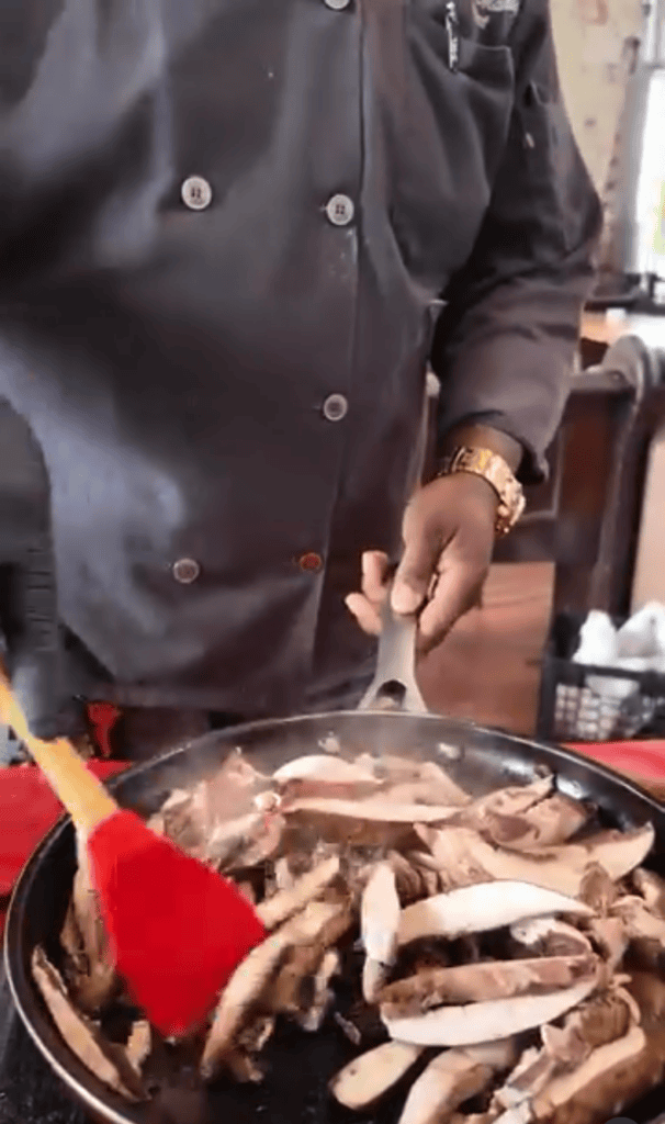 A person in dark clothing prepares fresh crabs in a large pot outdoors during daytime cooking.