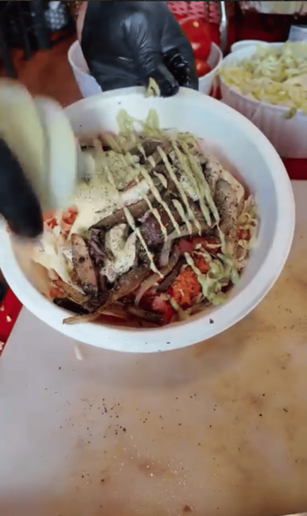 A close-up overhead view of a plated noodle dish topped with mayo drizzle and red sauce, served in a white bowl at a casual dining setting.
