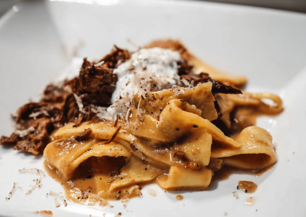 A close-up shot of a golden waffle topped with chocolate shavings and powdered sugar served on a white plate.