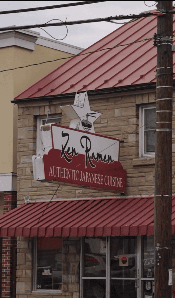 A brick storefront restaurant with a red metal roof and striped awning displays signage for an authentic dining establishment.
