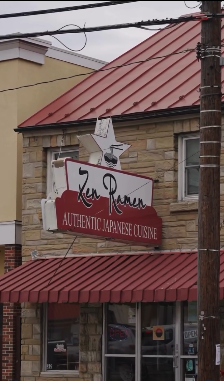 A brick storefront restaurant with a red metal roof and striped awning displays signage for an authentic dining establishment.