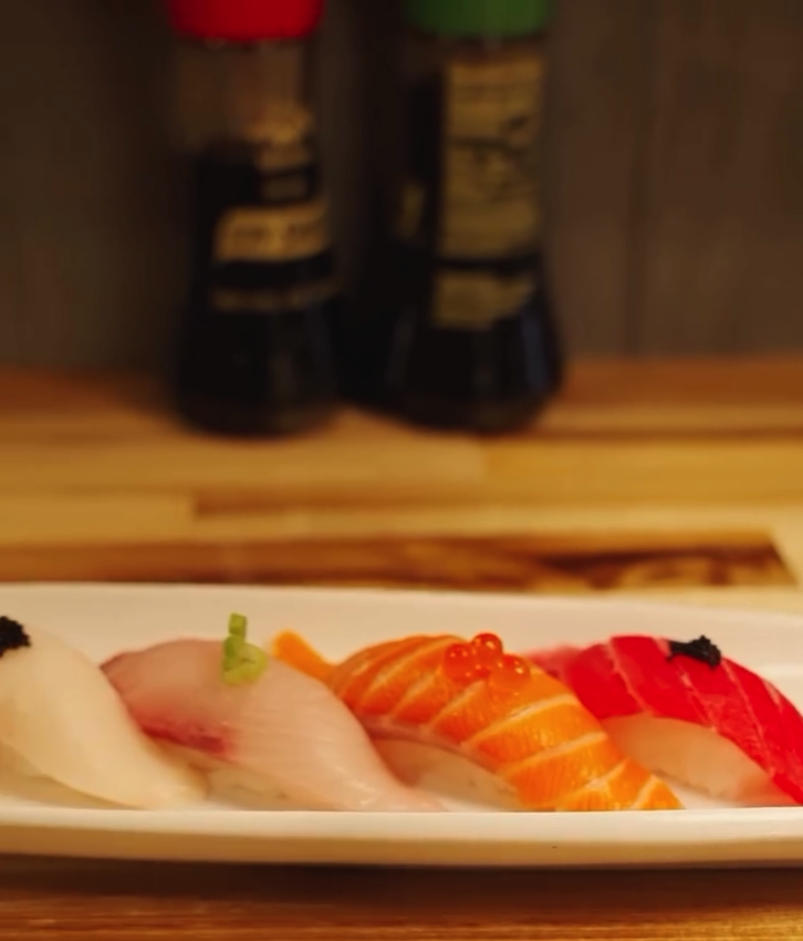A beautifully plated sushi assortment featuring various types of nigiri arranged in a line on a white plate in a warm-lit restaurant setting.