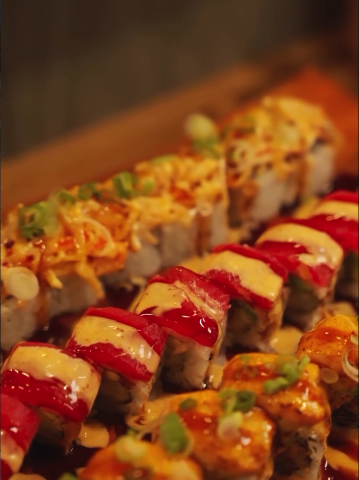 An appetizing close-up of artfully plated sushi rolls garnished with colorful toppings including red ginger, sesame seeds, and green onions.