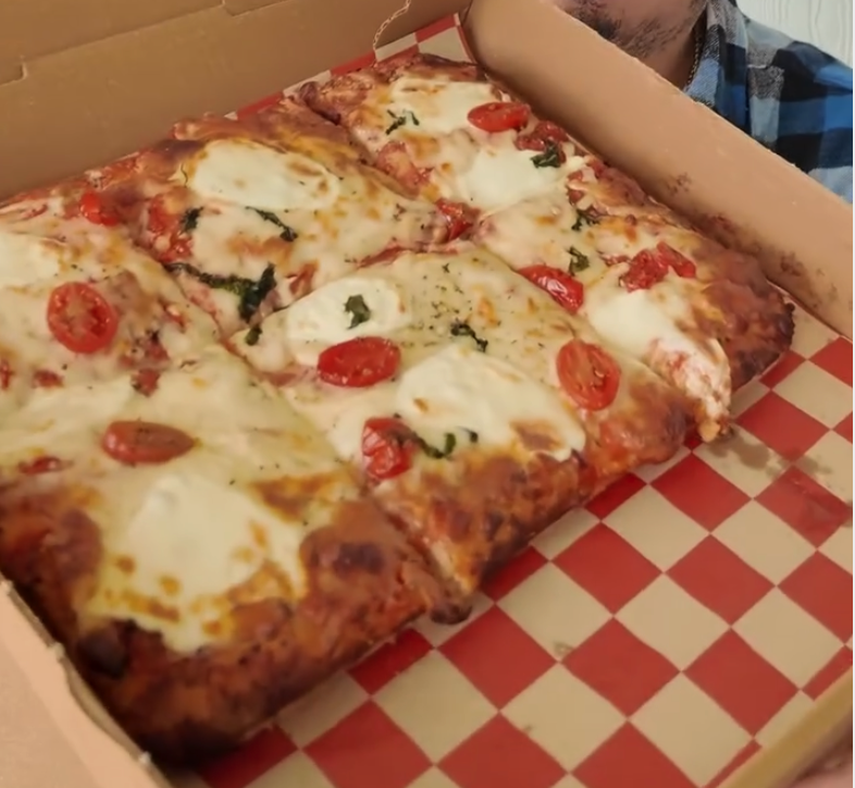 A fresh pepperoni and cheese pizza sits in an open cardboard box lined with red checkered paper, ready to be served.