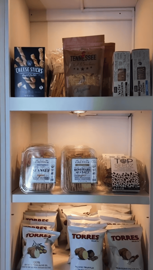 A three-shelf retail display cabinet showcasing various books, beverages, and packaged products with warm ambient lighting.