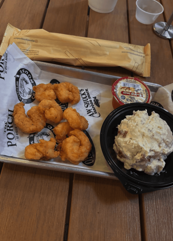 An overhead view of a plated fried shrimp dish served on a wooden board with coleslaw and dipping sauce at what appears to be a restaurant.