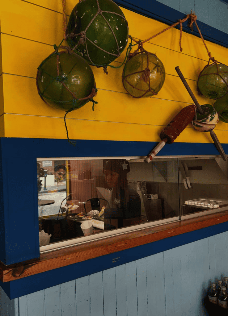 A workshop or craft space displays dried gourds hanging from a yellow wall above a display window showing interior workspace activity.