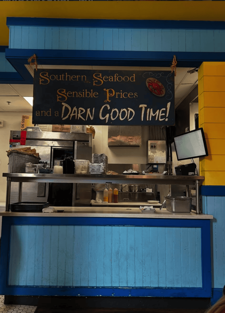 A small seafood market stall with a chalkboard menu advertising fresh catches and daily specials, framed by blue trim and yellow signage.