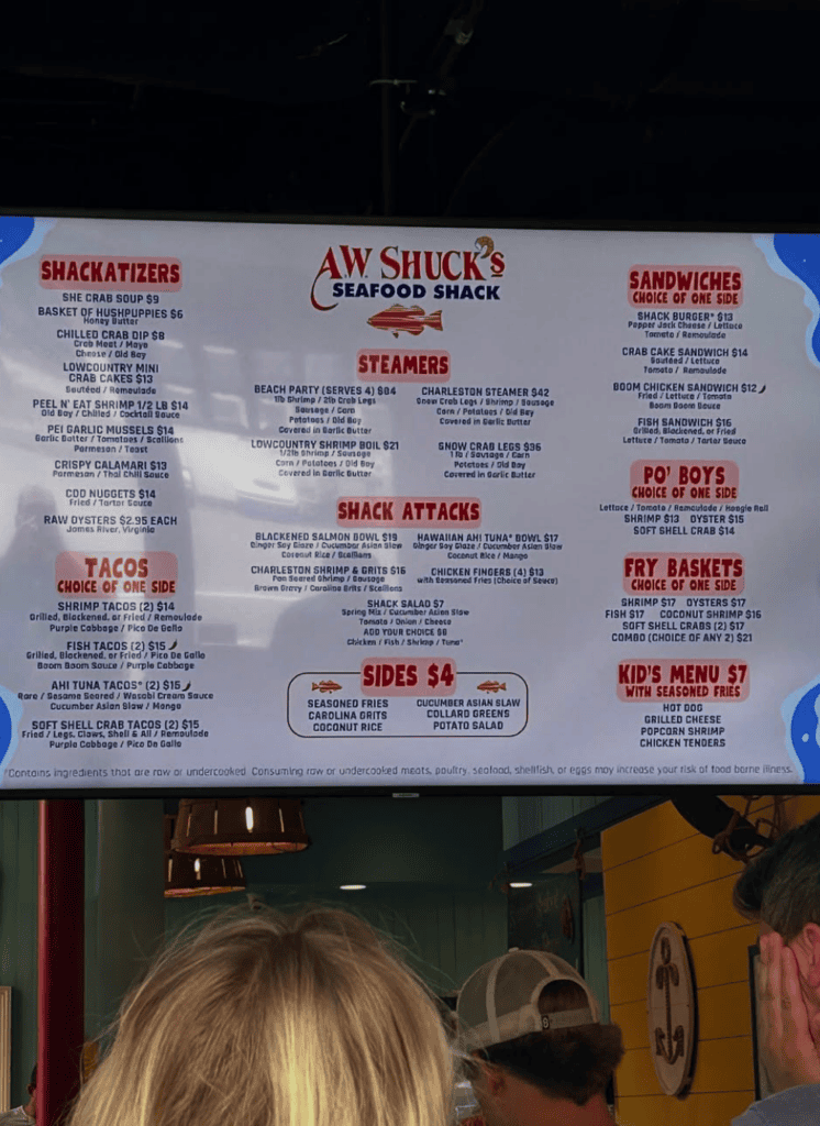 A person views a restaurant menu board displaying food items and prices in a dimly lit indoor venue.