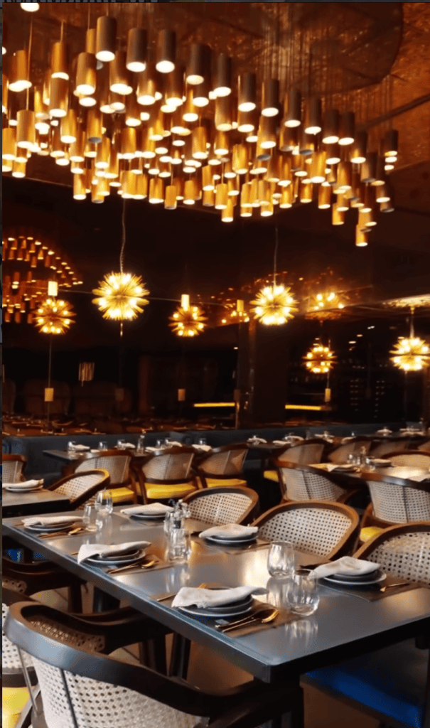 An elegantly decorated upscale dining venue featuring warm golden pendant lights suspended from the ceiling and formally set tables below.