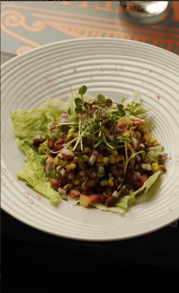A elegantly plated salad with mixed greens, roasted beets, and nuts served on a white ribbed plate in an indoor dining setting.