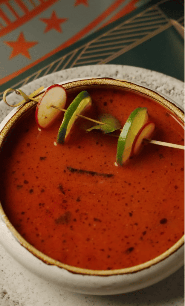 A vibrant red tomato soup served in a decorative ceramic bowl, garnished with fresh green onion slices, photographed from above in warm indoor lighting.