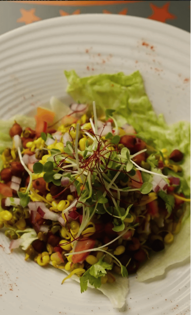 A vibrant, artfully plated salad with mixed greens, colorful vegetables, and delicate microgreens arranged on a white textured plate.