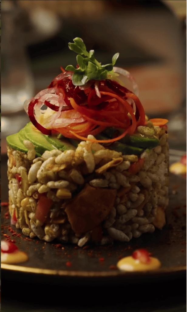An elegantly plated fine dining dish featuring a lentil base topped with sliced prosciutto, fresh microgreens, and rich sauce garnish.