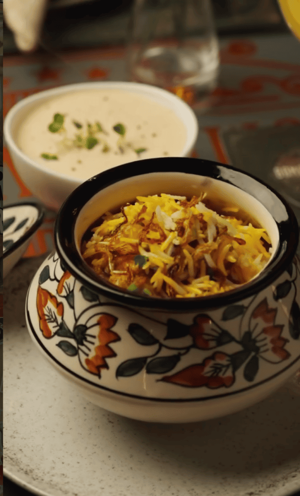 A close-up of a steaming bowl of golden curry noodles served in a decorative ceramic bowl with floral patterns on a dining table.