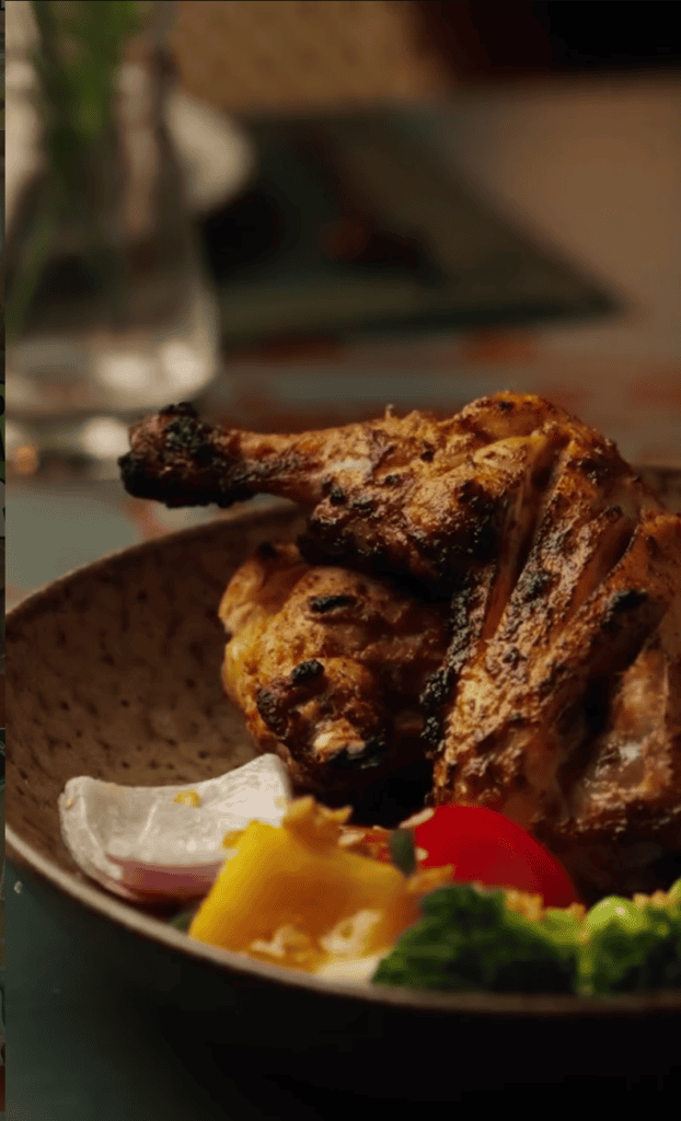 Golden-brown fried chicken pieces are plated with fresh lemon wedges, red peppers, and green lettuce in an appetizing close-up food photography shot.