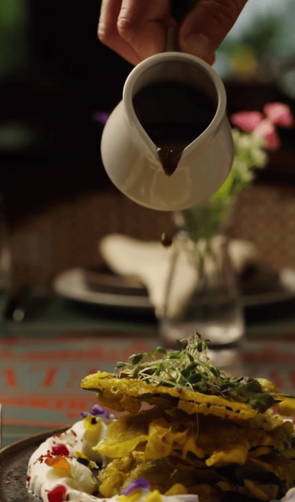 A chef waters a plated dish with a small watering can in a garden setting, creating an artistic food presentation.