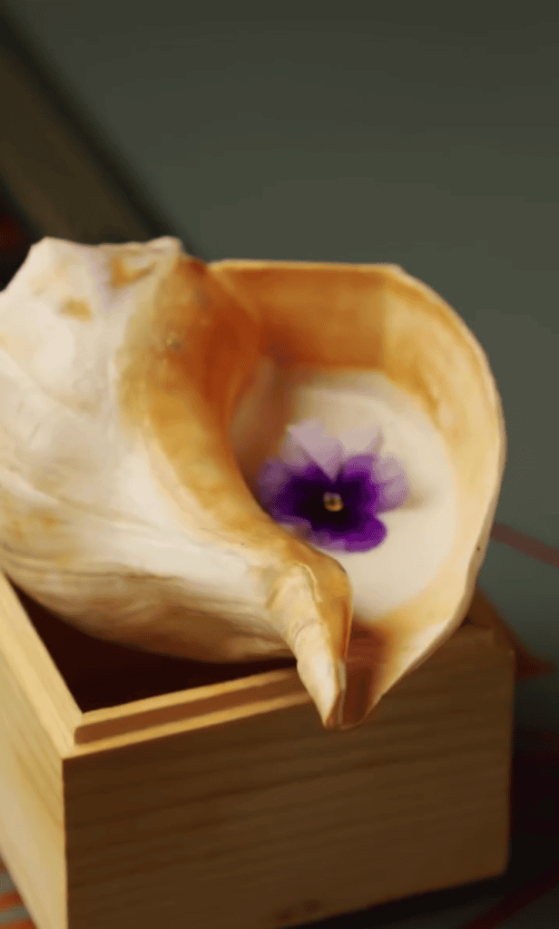 A delicate white calla lily with a striking purple center rests on a wooden box, captured in soft studio lighting.