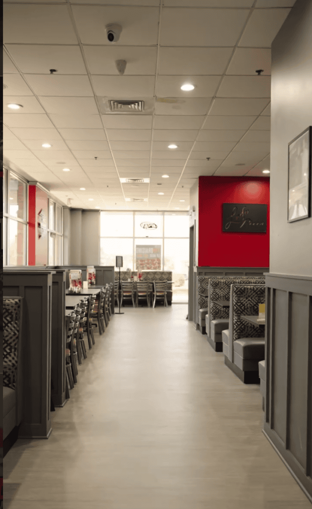 A clean, well-lit indoor commercial dog kennel facility with multiple metal crates lining both sides of a hallway and red artwork on the wall.
