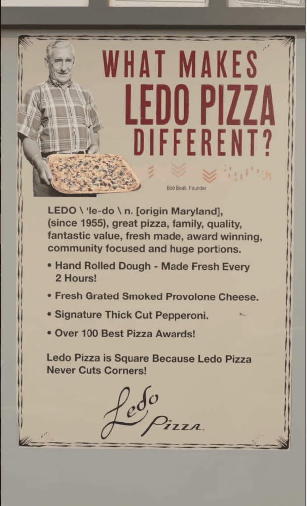 A framed Ledo Pizza promotional sign featuring a man in a plaid shirt, pizza image, descriptive text about what makes Ledo Pizza different, and a handwritten signature at the bottom.