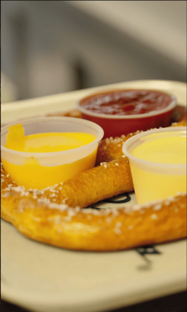 A close-up of golden fried pastries served with yellow custard sauce and red jam on a white plate.
