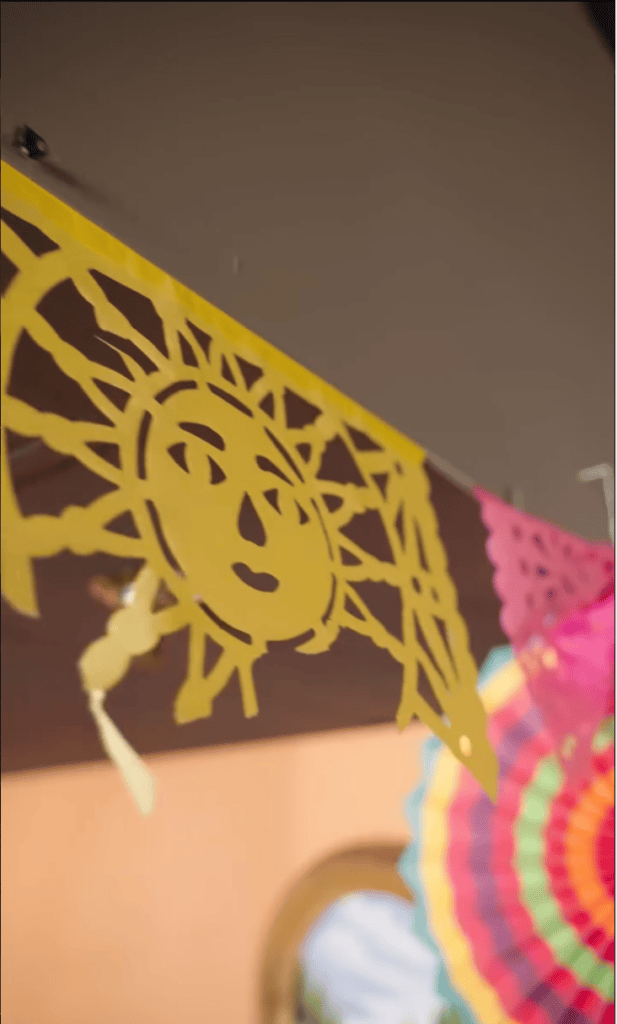 A close-up view of yellow and pink papel picado, a traditional Mexican decorative paper banner with intricate cut-out designs.