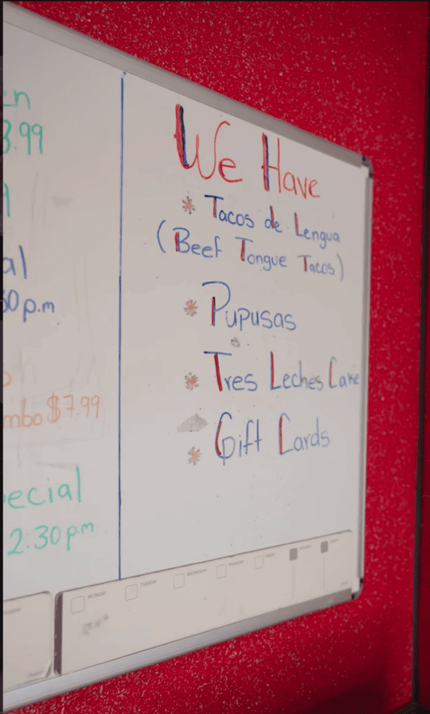 A whiteboard with handwritten text and notes mounted on a deep red wall, featuring various words and phrases written in marker.