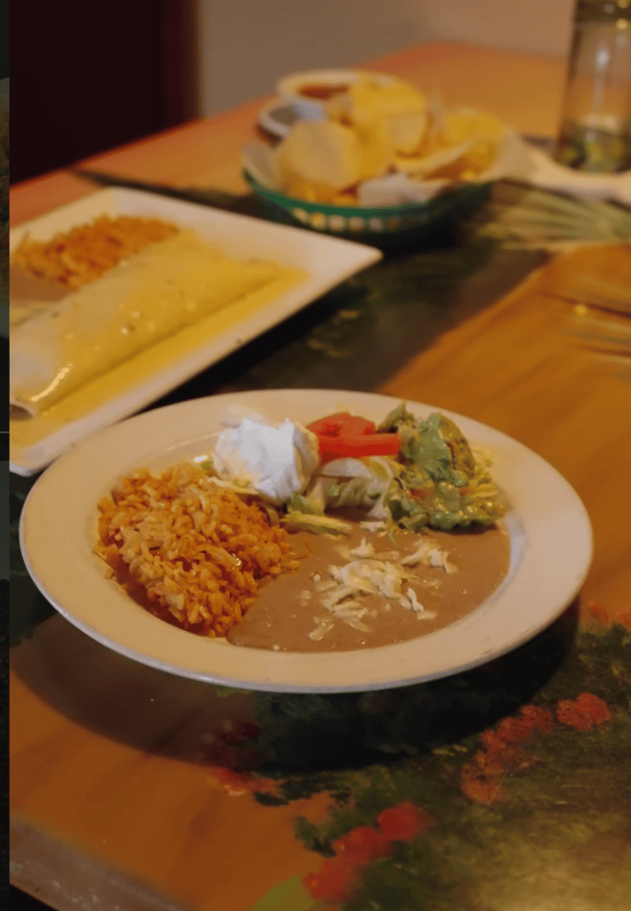 A plated dinner featuring a golden potato pancake with sauce and fresh vegetables served on white dinnerware at a wooden dining table.
