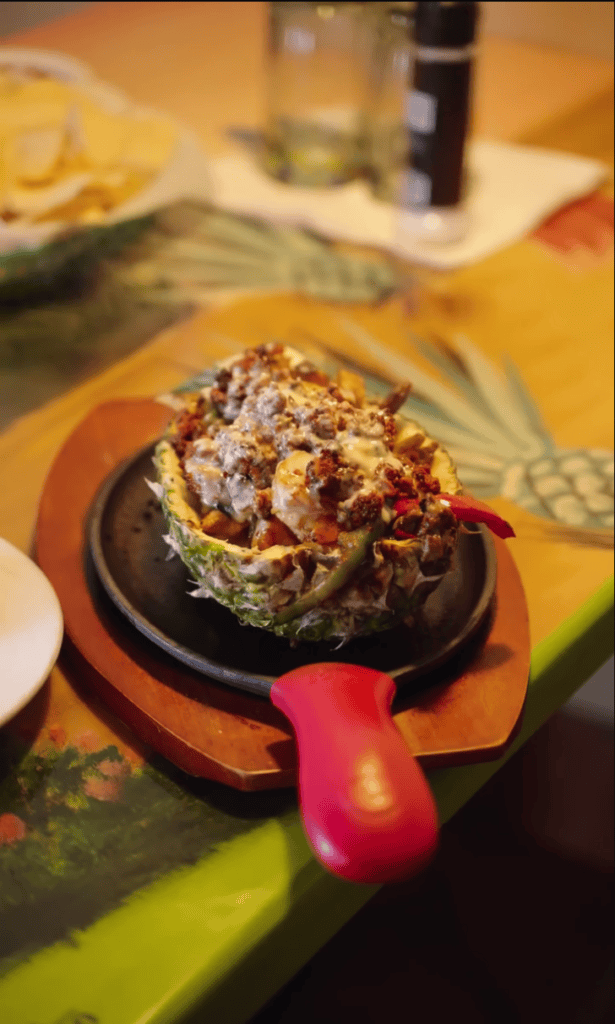 A close-up of a stuffed mushroom appetizer served in a small skillet on a dining table with other food and tableware visible in the background.