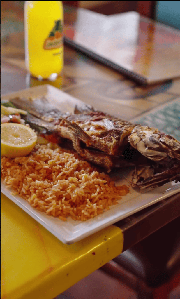 Grilled meat skewers served on a white plate with a golden sauce, accompanied by a yellow condiment bottle on a wooden table.