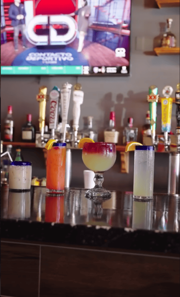 A beautifully organized collection of colorful cosmetic and fragrance bottles displayed on a dark shelf, showcasing nail polish, perfumes, and other beauty products in jewel-toned hues.