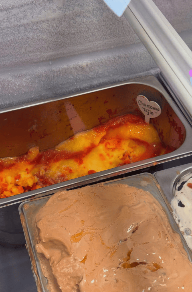 Close-up view of food service containers holding baked items with orange-golden coloring and a tan-colored spread or frosting.