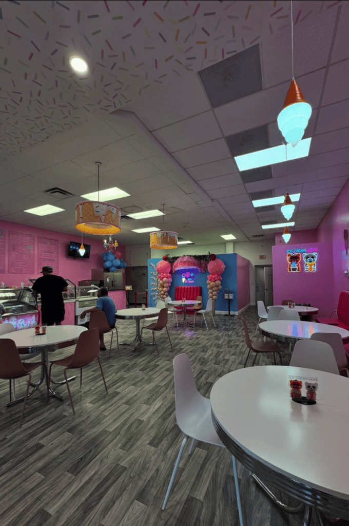 A vibrant indoor recreation center with arcade games, ping pong tables, and neon pink and blue lighting creates an energetic entertainment space.
